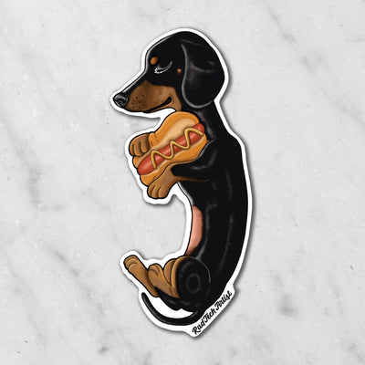 Magnet of a black and tan dachshund holding a hot dog on a marble surface
