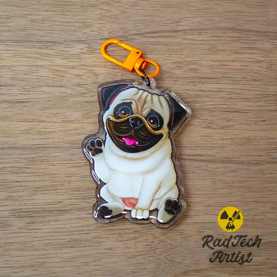 Acrylic fawn Pug keychain with epoxy finish, featuring a playful dog waving its paw. Attached to an orange lobster clasp, displayed on a warm wood background.