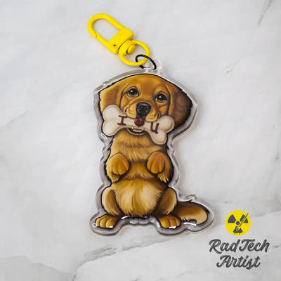 Acrylic Golden Retriever keychain with epoxy finish, featuring a golden pup holding a bone that says “I ❤️ U.” Attached to a yellow lobster clasp, displayed on a marble background with the Rad Tech Artist logo.