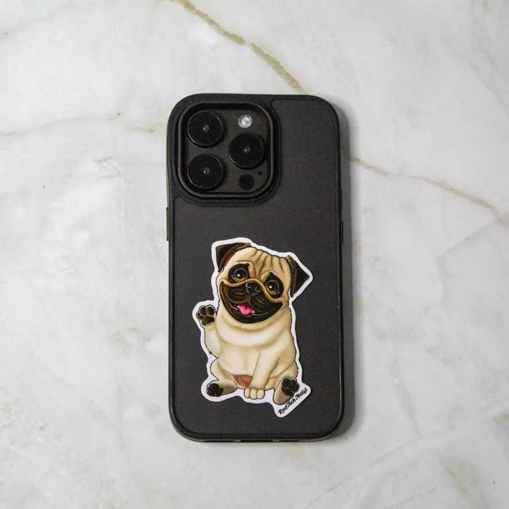 Photo of a fawn pug vinyl sticker with a raised paw and happy expression, placed on a black iPhone case against a light marble background.