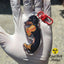 Black and tan Dachshund acrylic keychain with epoxy finish, featuring a playful pup holding a hot dog. Attached to a red lobster clasp and held in a gloved hand under sunlight, with the Rad Tech Artist logo in the corner.