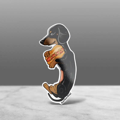 A sticker of a Black and Tan dachshund sleeping and holding a hot dog pillow with a happy expression.
