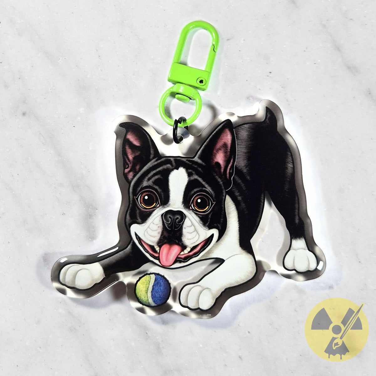 A custom acrylic keychain featuring a cartoon Boston Terrier dog holding a tennis ball, attached to a bright green swivel clasp, on a light gray marble background.