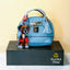 Blue textured handbag with a Boxer puppy keychain on a black stand against a yellow background