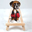 Sticker of a fawn boxer puppy wearing red boxing gloves on a small wooden easel against a white background