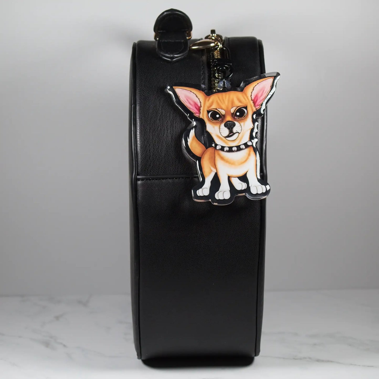 Black handbag with a fawn chihuahua dog keychain on a light gray background