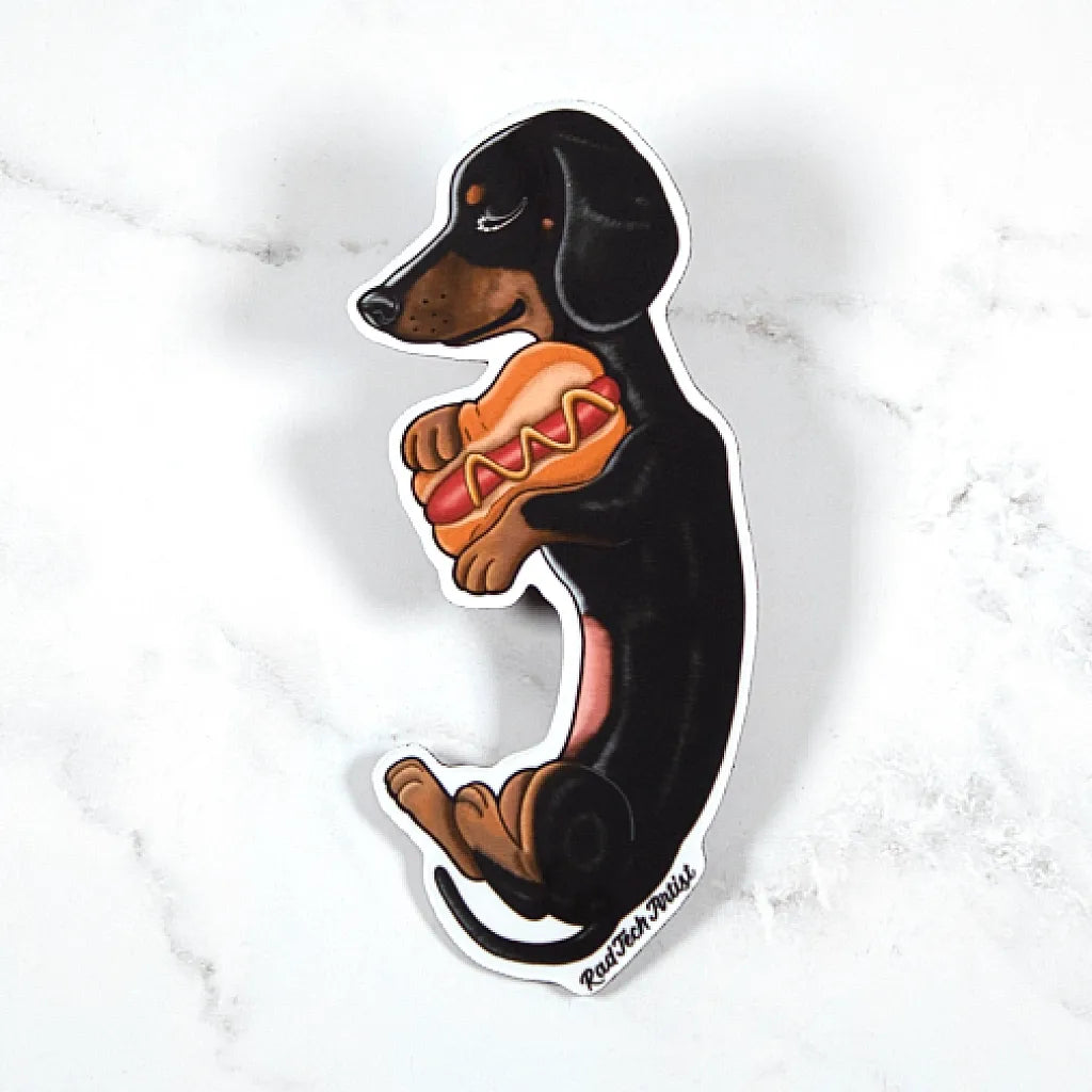 Magnet of a black and tan dachshund holding a hot dog on a marble background