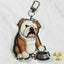 A custom acrylic keychain shaped like a bulldog sitting next to a metal bowl, shown on a light marble background.