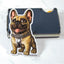 Sticker of a fawn French Bulldog with a chain leaning up against a blue wallet on a white marble background