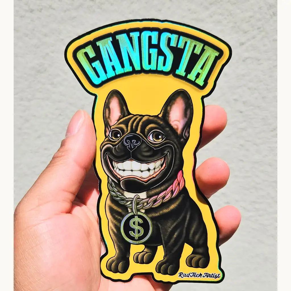 Hand holding a holographic vinyl sticker of a French Bulldog with a huge toothy grin, wearing a thick gold chain with a large dollar sign pendant. The sticker features bold, holographic "GANGSTA" text at the top and a bright yellow background. The holographic shine adds rainbow effects to the gold elements and lettering. "Rad Tech Artist" is printed in the bottom corner.