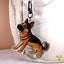 A die-cut acrylic keychain featuring a detailed illustration of a German Shepherd dog, shown hanging from a black U-shaped clasp on a white backpack.