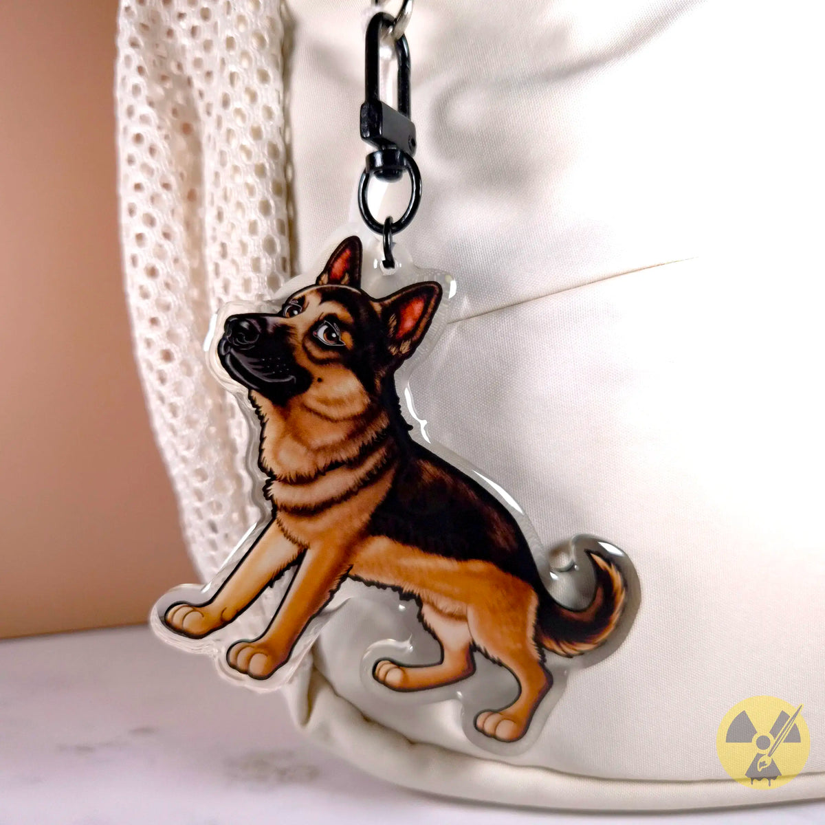 A die-cut acrylic keychain featuring a detailed illustration of a German Shepherd dog, shown hanging from a black U-shaped clasp on a white backpack.