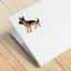 Mock-up image of a black and tan German Shepherd sticker placed on the back of a silver laptop. The dog stands alert with a confident stance and upright ears. The laptop rests on a light wood surface.