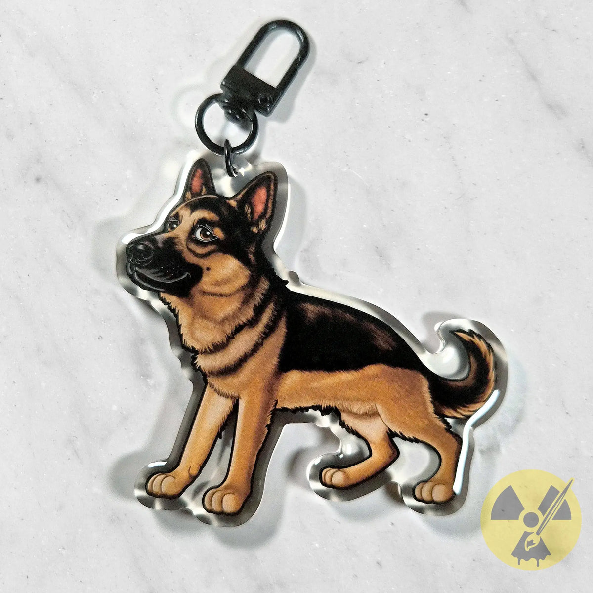 A die-cut acrylic keychain charm shaped like a German Shepherd dog, featuring a detailed illustration of the dog in black and tan, attached to a black metal lobster clasp, shown on a light marble background.