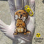 Golden Retriever acrylic keychain with epoxy finish, showing a golden pup holding a bone that says “I ❤️ U.” Attached to a yellow lobster clasp and held in a gloved hand under sunlight, with the Rad Tech Artist logo in the corner.