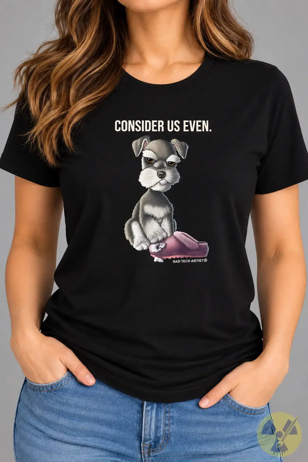 A woman wearing a black graphic t-shirt with a cartoon Schnauzer sitting on a pink slipper and the text 'CONSIDER US EVEN.' above it, paired with blue jeans.