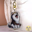 A die-cut acrylic keychain charm featuring an illustrated whining husky dog wearing a purple collar labeled 'Drama Queen' with a gold clasp, shown hanging against a white textured bag.