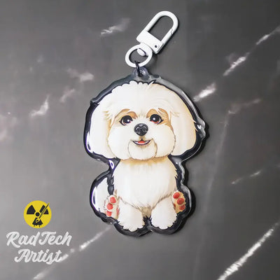 Maltese acrylic dog keychain photographed on a gray background, featuring a white coat illustration and silver lobster clasp.