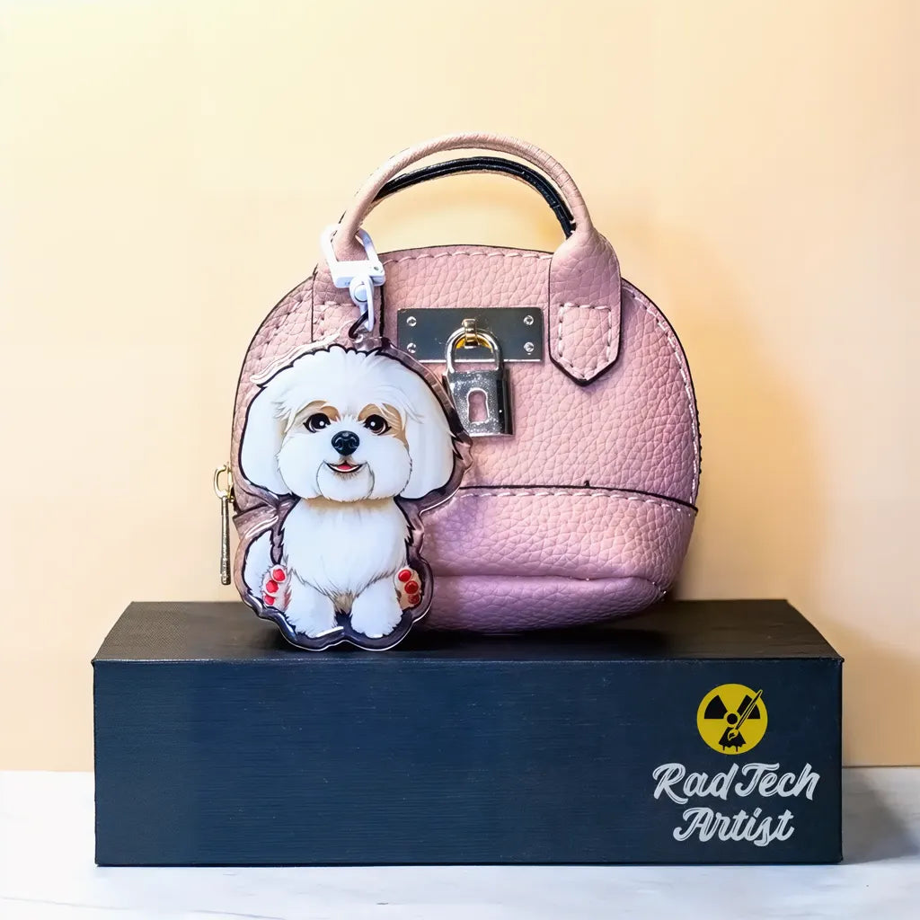 Maltese dog acrylic keychain with a white coat design attached to a pink handbag, displayed on a black stand.