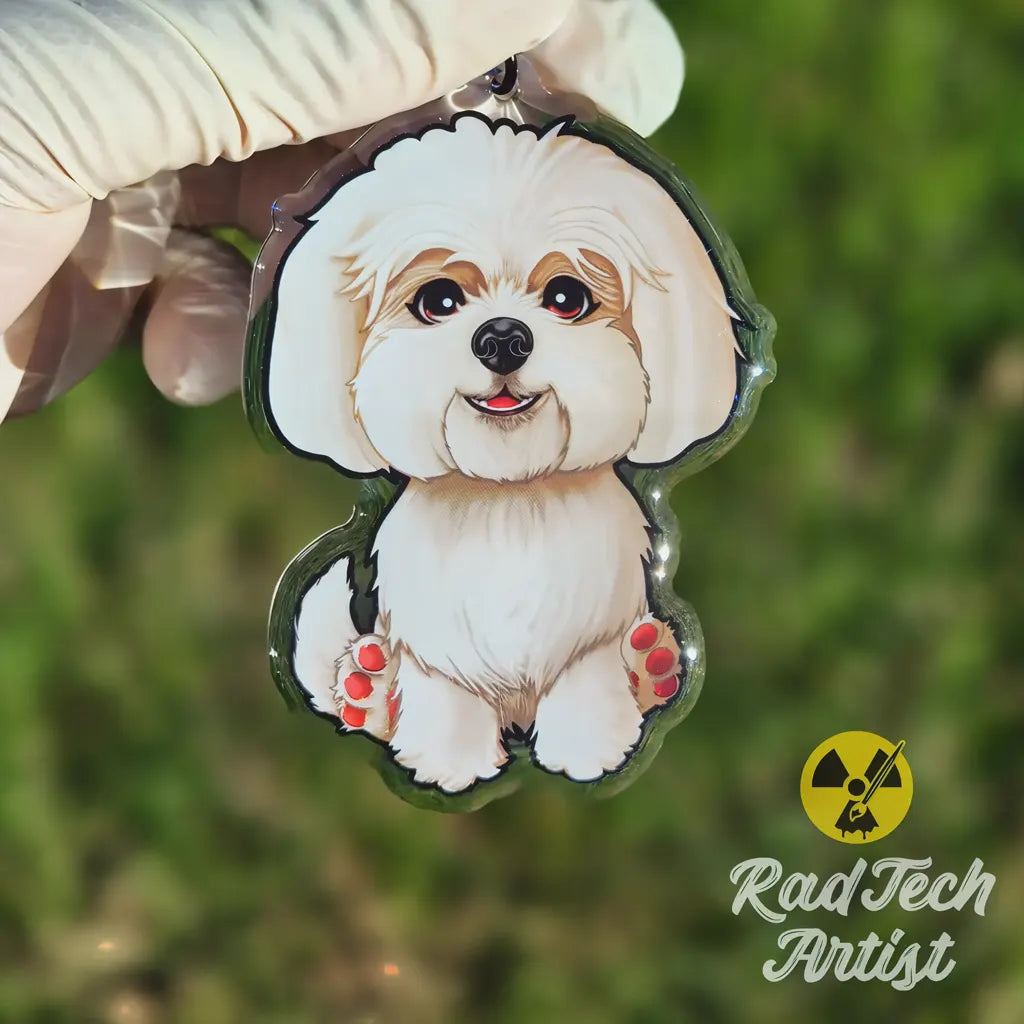 Close-up of a Maltese acrylic keychain held in hand, showing the smiling white dog illustration and glossy epoxy surface.