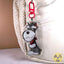 A cartoon-style Miniature Schnauzer dog keychain charm with a red collar and red clasp, shown hanging against a white textured bag.