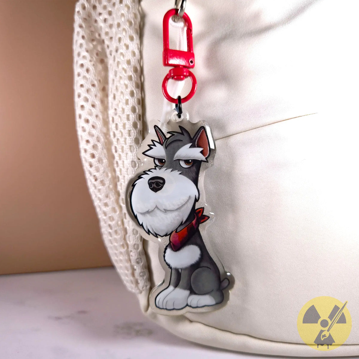 A cartoon-style Miniature Schnauzer dog keychain charm with a red collar and red clasp, shown hanging against a white textured bag.
