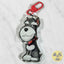 A cartoon dog-shaped acrylic keychain charm featuring a salt-and-pepper Miniature Schnauzer dog with a red bandana and red clasp, photographed on a light marble surface.