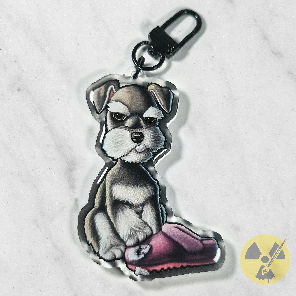Photo of a miniature schnauzer puppy keychain with a chewed pink slipper hanging on a marble surface.