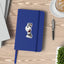 Mock-up image of a salt and pepper Miniature Schnauzer sticker placed on the cover of a blue notebook. The Schnauzer has a sly smile and wears a red bandana. The notebook sits on a light wood desk beside a black pen, an open latte, and a small green plant.