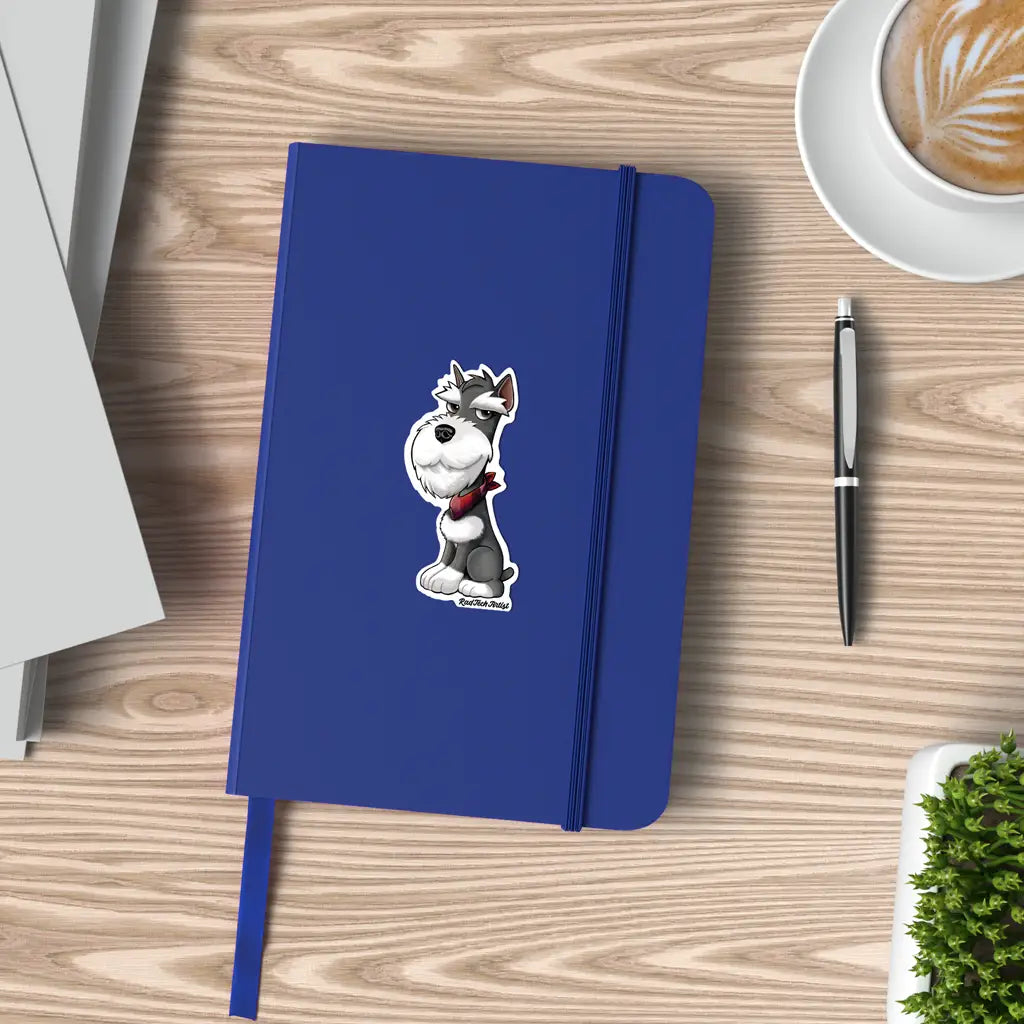 Mock-up image of a salt and pepper Miniature Schnauzer sticker placed on the cover of a blue notebook. The Schnauzer has a sly smile and wears a red bandana. The notebook sits on a light wood desk beside a black pen, an open latte, and a small green plant.