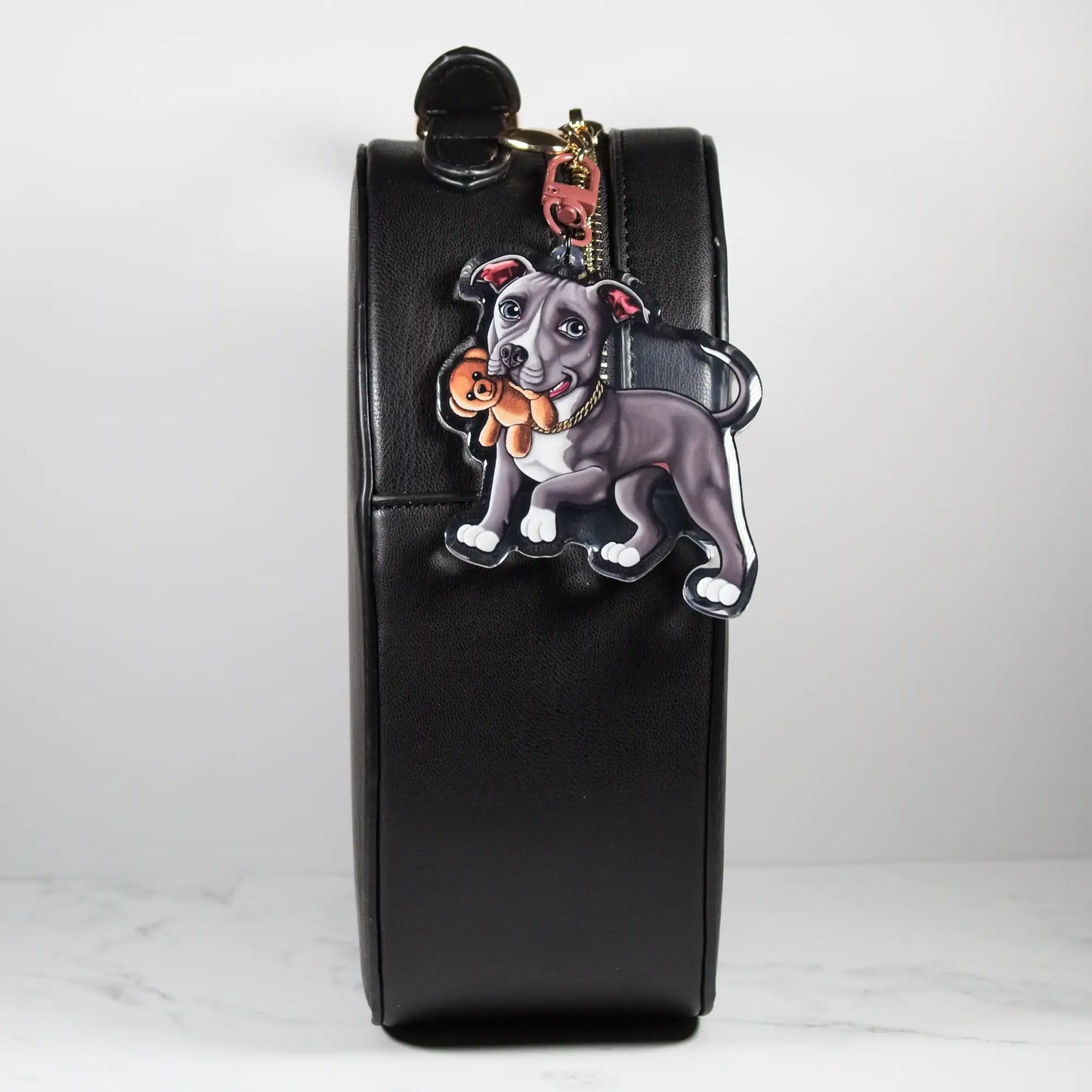 Black leather bag with a blue and white Pit Bull keychain on a white background