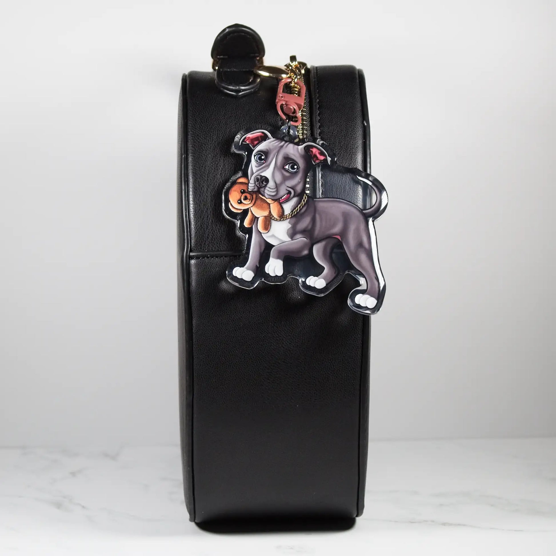 Black leather bag with a blue and white Pit Bull keychain on a white background
