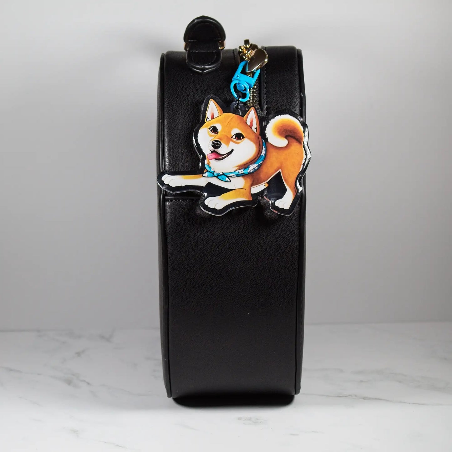 Black leather pouch with a red Shiba Inu dog keychain on a white marble surface