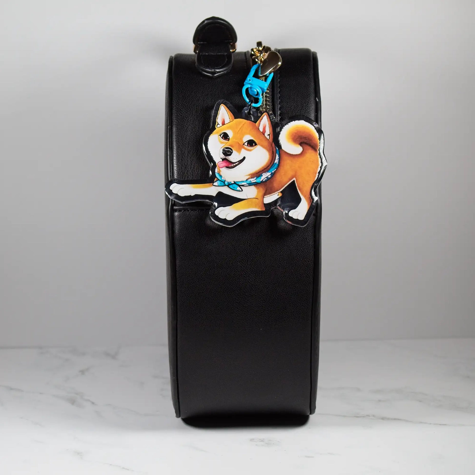 Black leather pouch with a red Shiba Inu dog keychain on a white marble surface