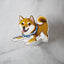 Shiba Inu dog magnet with red coat and blue bandana displayed on a glass stand over a marble background.