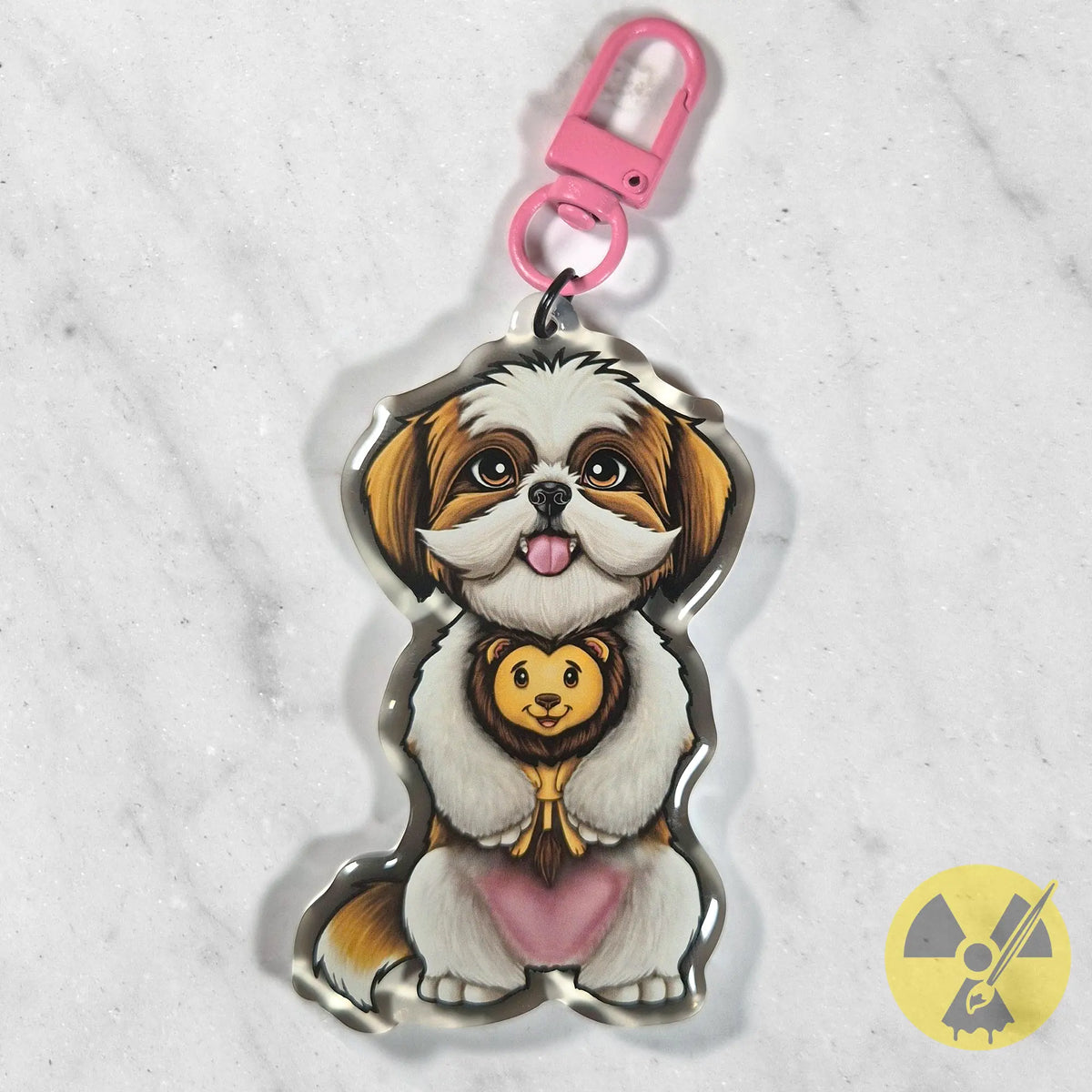 A custom acrylic keychain charm shaped like a Shih Tzu holding a small lion plush toy, with a pink lobster clasp at the top, displayed on a white marble background.