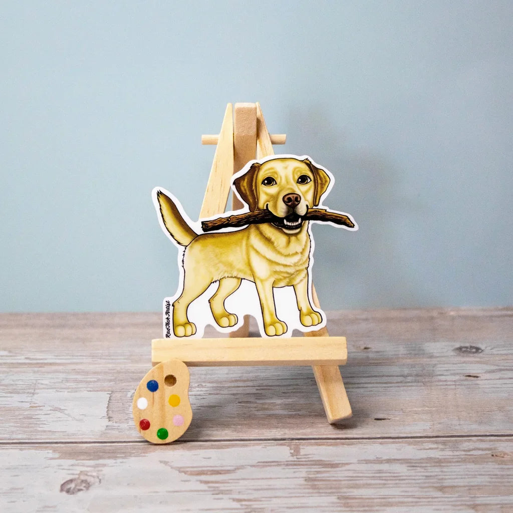Vinyl dog sticker of a yellow Lab holding a stick on brown surface – waterproof Labrador sticker for dog lovers.