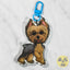 A custom acrylic keychain shaped like a Yorkshire Terrier dog, featuring a bright blue metal clasp at the top. The dog illustration has tan and gray fur with pink inner ears and a small pink tongue.