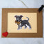 Actual photo of a blue American Pit Bull Terrier vinyl sticker placed on a bordered card. The pit bull has a sweet expression and is holding a teddy bear in its mouth. The card is decorated with a red glitter heart in the bottom left corner and a small black dog cutout in the top right.