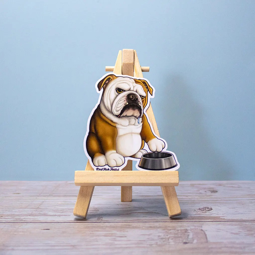 English Bulldog vinyl sticker displayed on a small wooden easel with a food bowl, set on a wooden surface against a soft blue background.