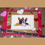 Photo of a sticker featuring a fawn male French Bulldog cuddling a black and white pied female French Bulldog with a pink bow. The sticker is centered on a layered background with glitter hearts, bone confetti, and “I love you” ribbon on a wooden surface.