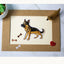 Photo of a black and tan German Shepherd vinyl sticker placed on a bordered card with bone confetti, a red glitter heart, and a miniature dog figure.