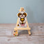 Vinyl sticker of a gold and white Shih Tzu sitting sweetly with a plush lion toy between its paws, displayed on a wooden easel with a blue background.