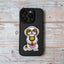 Photo of a gold and white Shih Tzu dog sticker with a sweet expression, holding a plush lion toy and sitting on a black iPhone case placed on a light wood background.