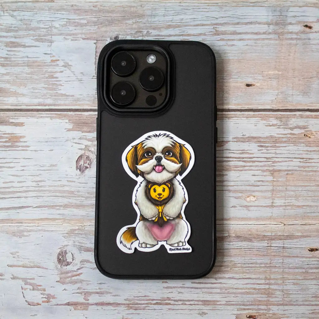 Photo of a gold and white Shih Tzu dog sticker with a sweet expression, holding a plush lion toy and sitting on a black iPhone case placed on a light wood background.